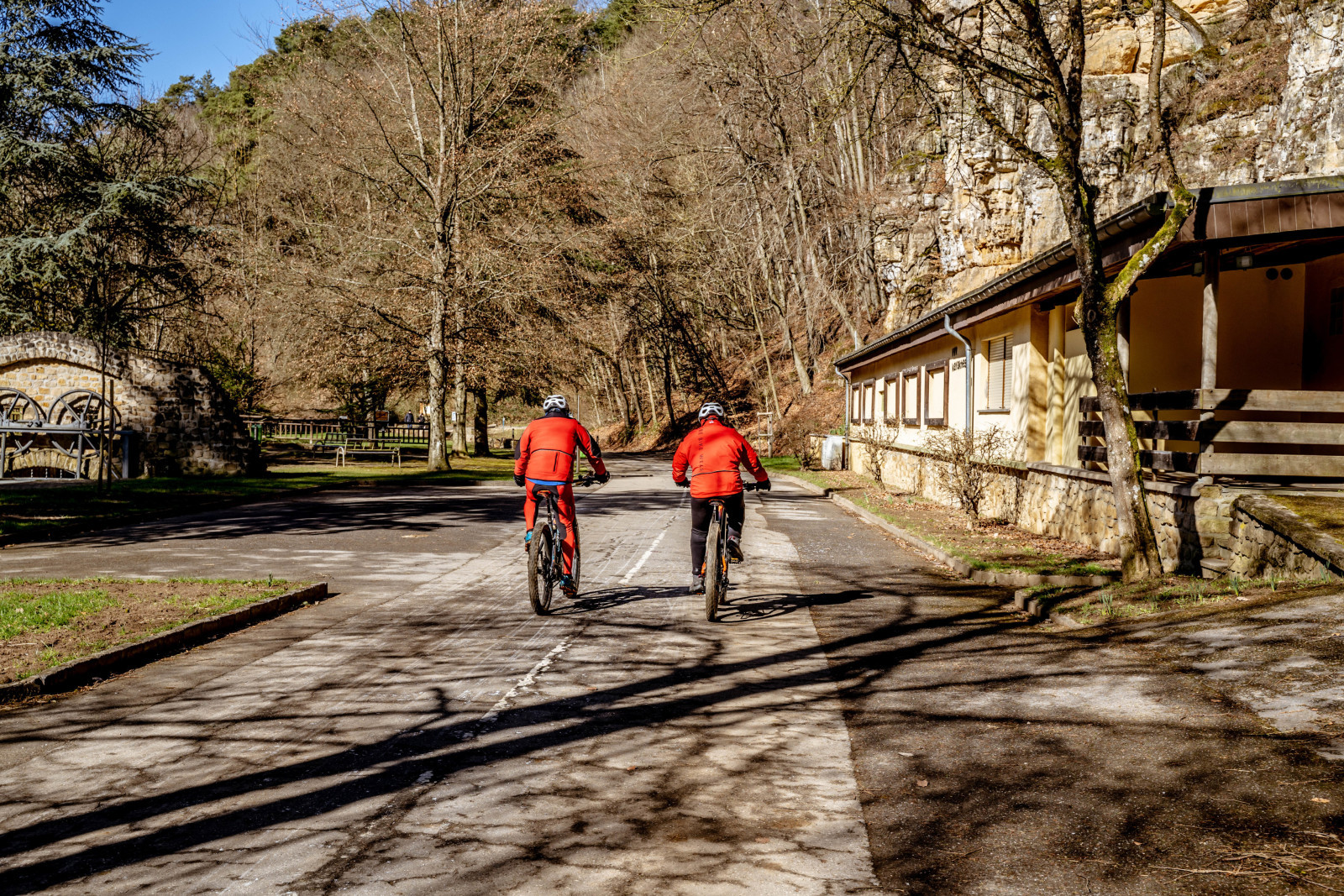 Zwei Radfahrer auf einem Weg im Alzette-Tal in Pulvermühl, umgeben von Felsen und Bäumen.