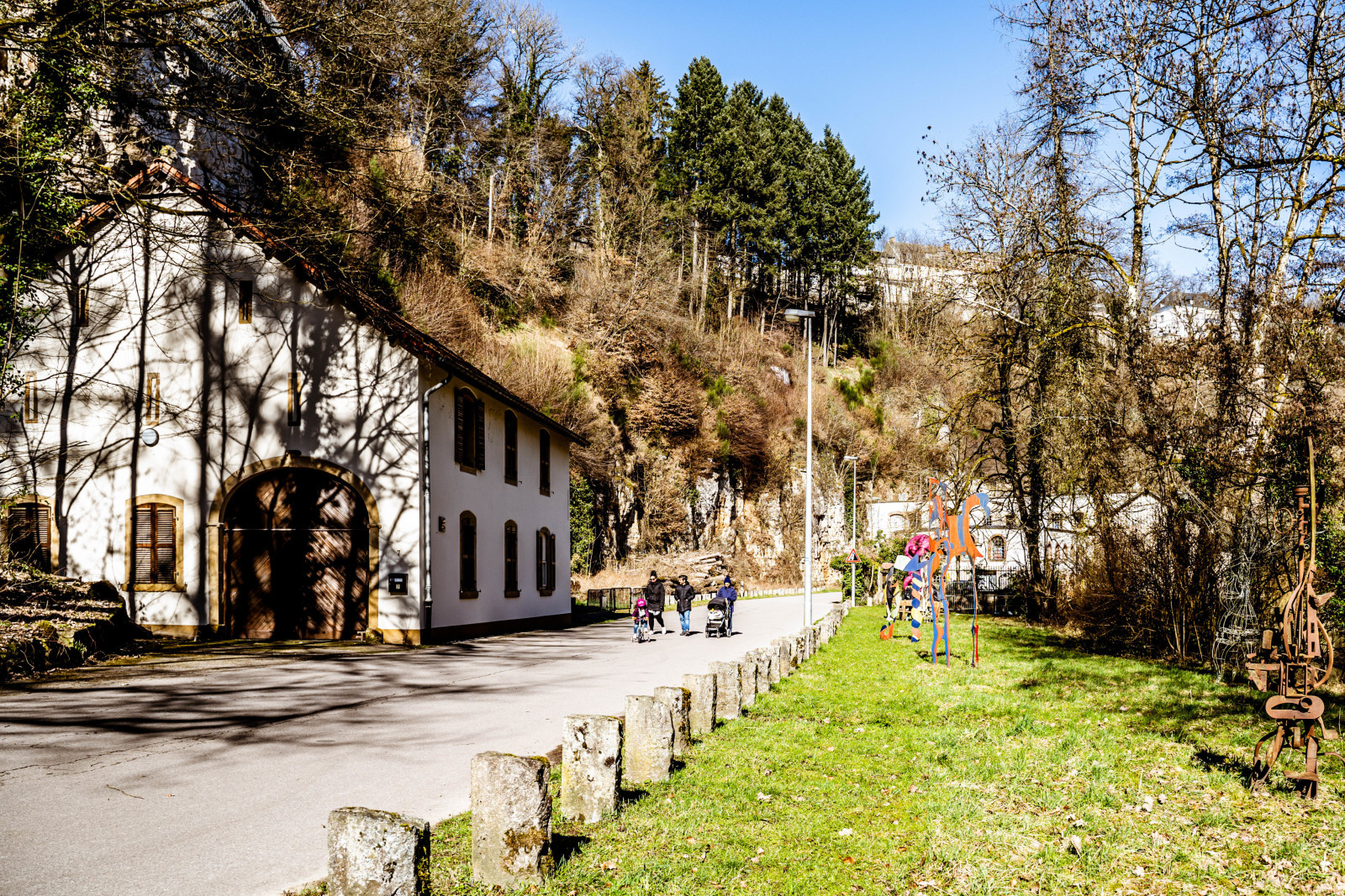 Chemin de promenade dans le quartier de Hamm, à Luxembourg-Ville, longeant la rivière Alzette et des maisons traditionnelles, entouré de verdure et de falaises.