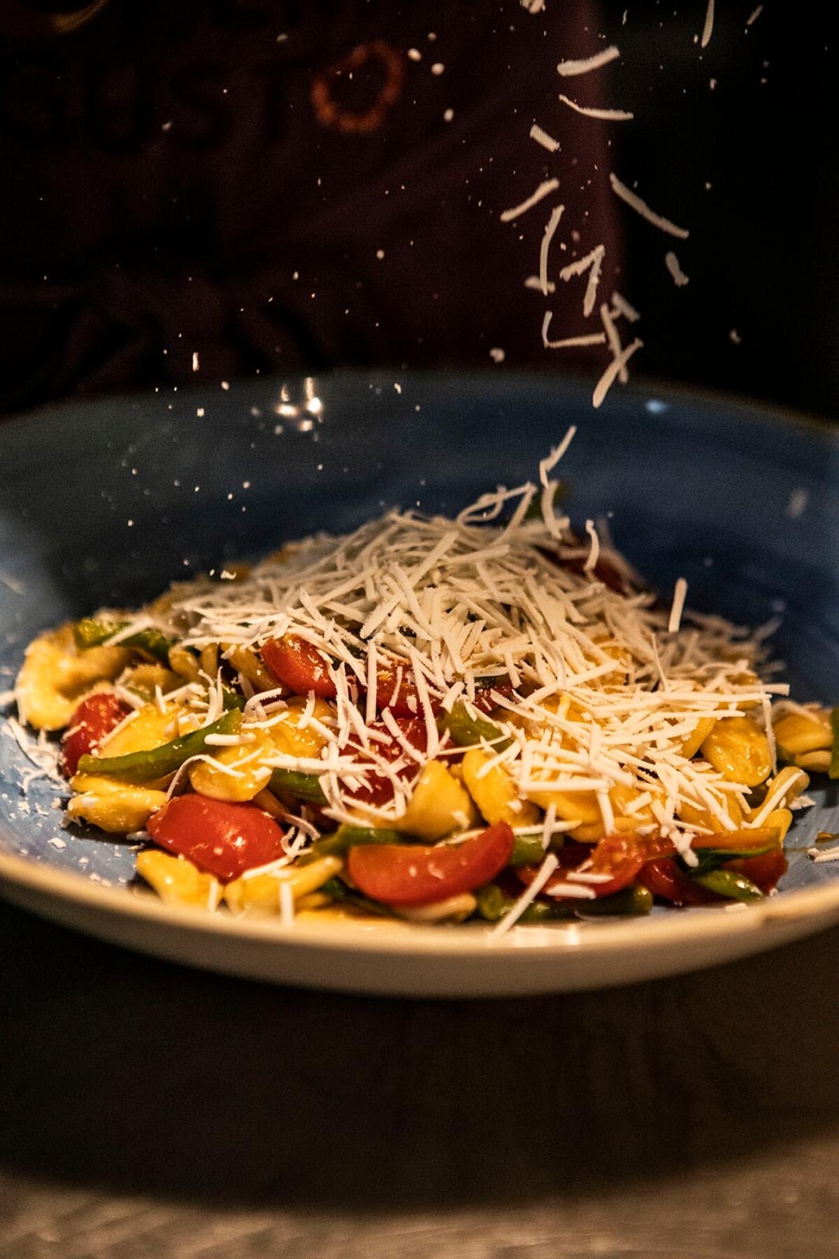 Blue bowl of pasta with cherry tomatoes, zucchini and parmesan shavings falling over the dish