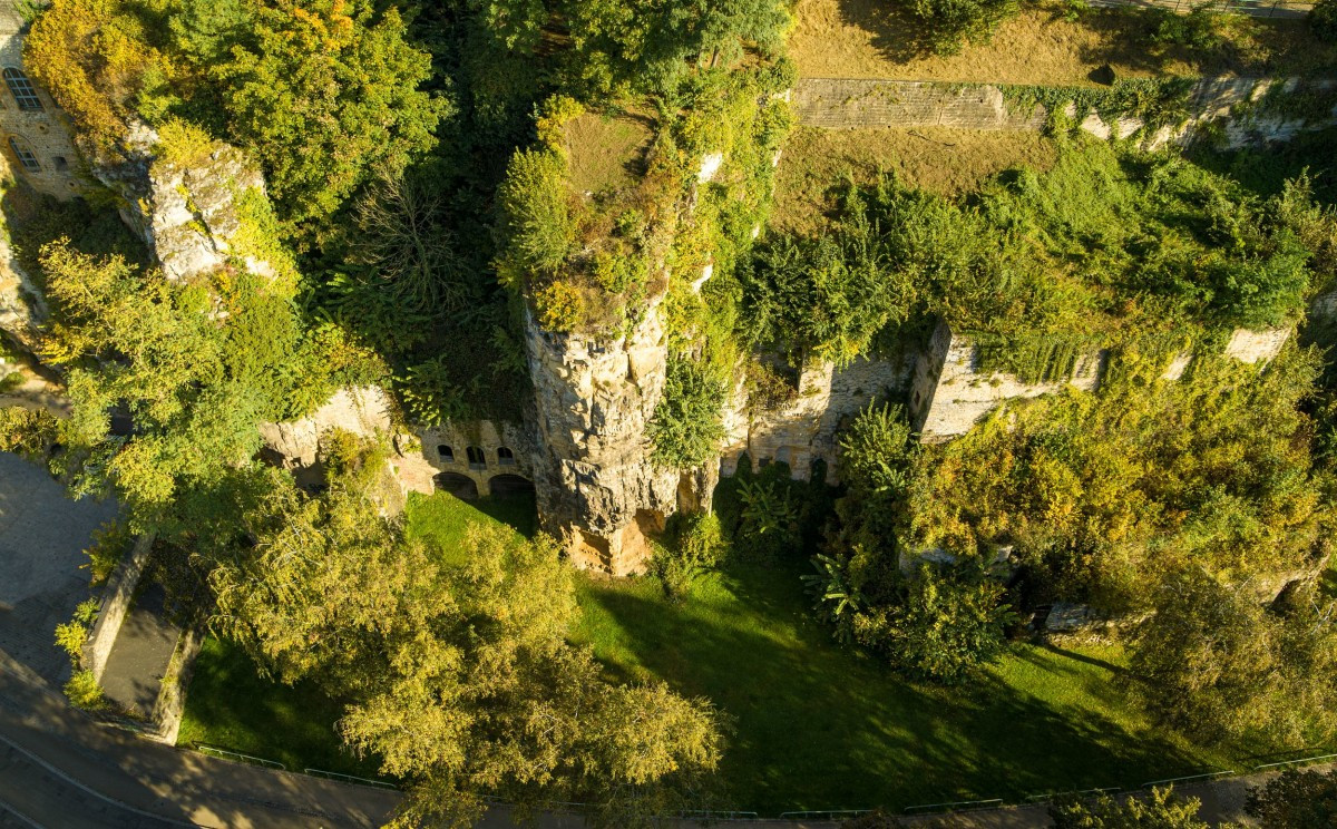Luftaufnahme der Ruinen und Überreste der Befestigungsanlagen im Petruss-Tal in Luxemburg, umgeben von Grünflächen und steilen Felsen.