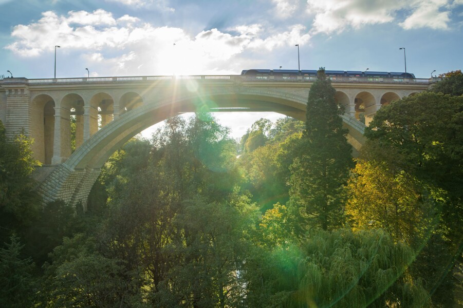Pont Viaduc dans la Vallée de la Pétrusse à Luxembourg-Ville, capturé en contre-plongée avec le soleil filtrant à travers les arbres.